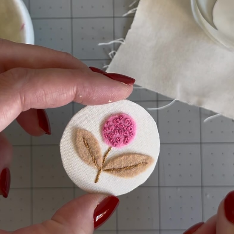 Wrapped circular panel with an embroidered pink flower and felt leaves